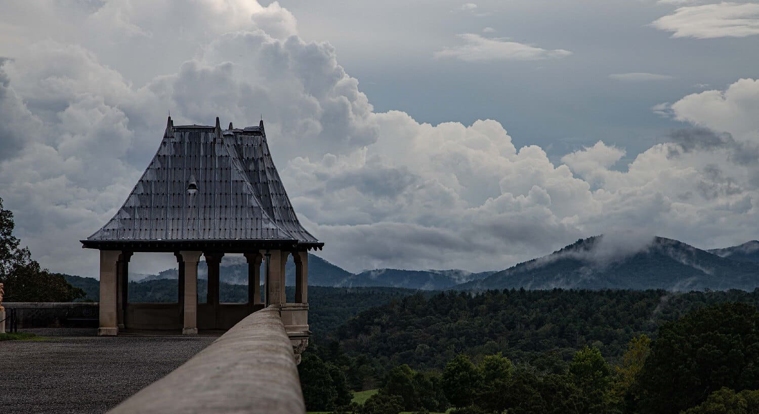 Gazebo at the corner of a walkway overlooking a vast forested mountain range under a cloudy sky