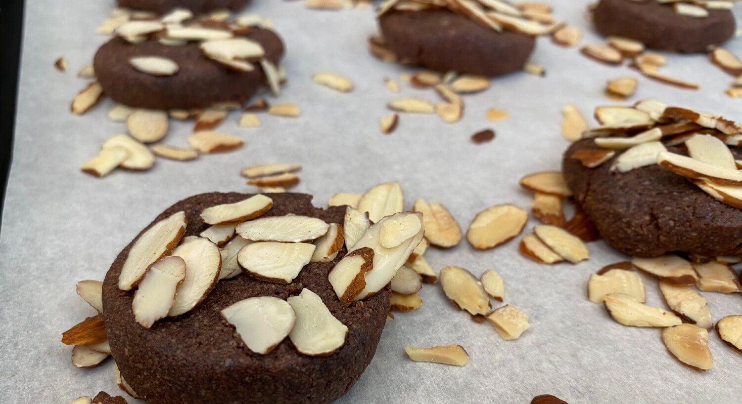 Parchment paper holding freshly baked brownie cookies covered in sliced almonds