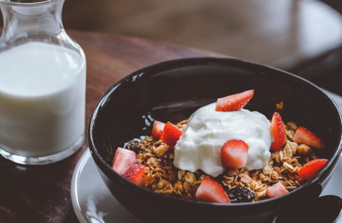 Small black bowl holding granola, berries and yogurt with small carafe of white milk
