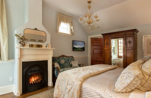 Cozy bedroom with white fireplace, king size bed, green sitting chair and tall mirrored armoire
