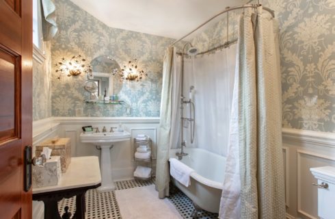 Beautiful antique bathroom with white clawfoot tub and round mirror over a pedestal sink