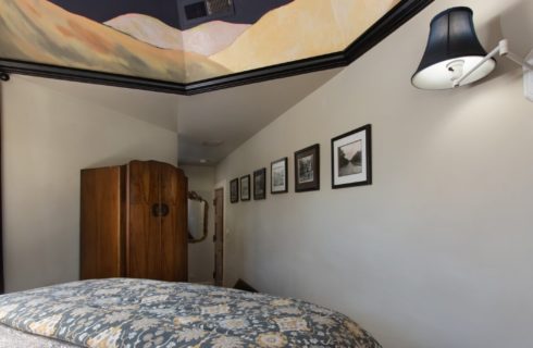 Hallway of a bedroom with a gallery wall of framed pictures, brown armoire and bed with flowered quilt