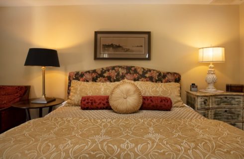 Plush king bed with flowered upholstered headboard, side tables with lamps and red sitting chair
