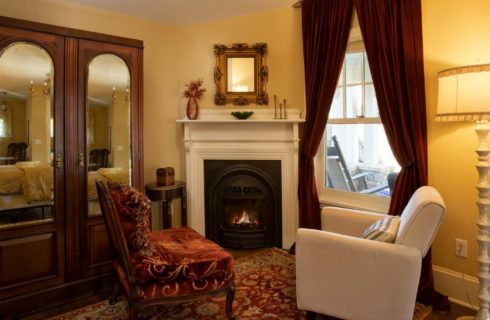 Two sitting chairs in front of a gas fireplace with a floor lamp and large mirrored armoire
