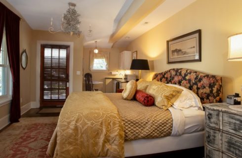King bed with floral headboard in bedroom with mini kitchenette and large windows