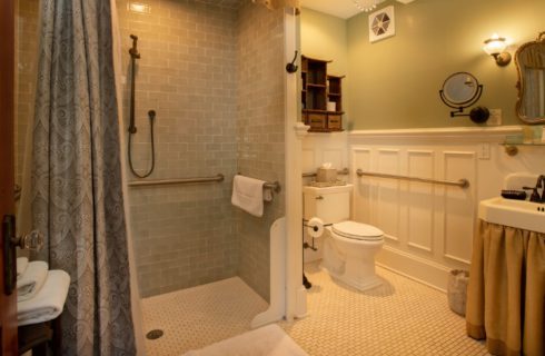 Spacious bathroom with roll in shower and white sink under large antique brass mirror