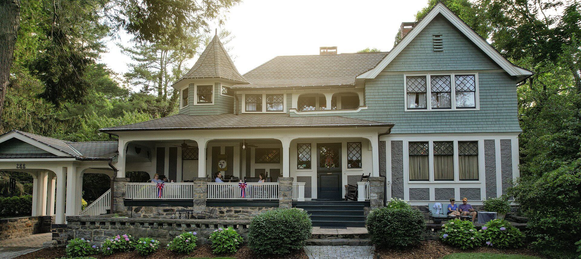 Front facade of a large home with porch, columns, side portico and lush landscaping