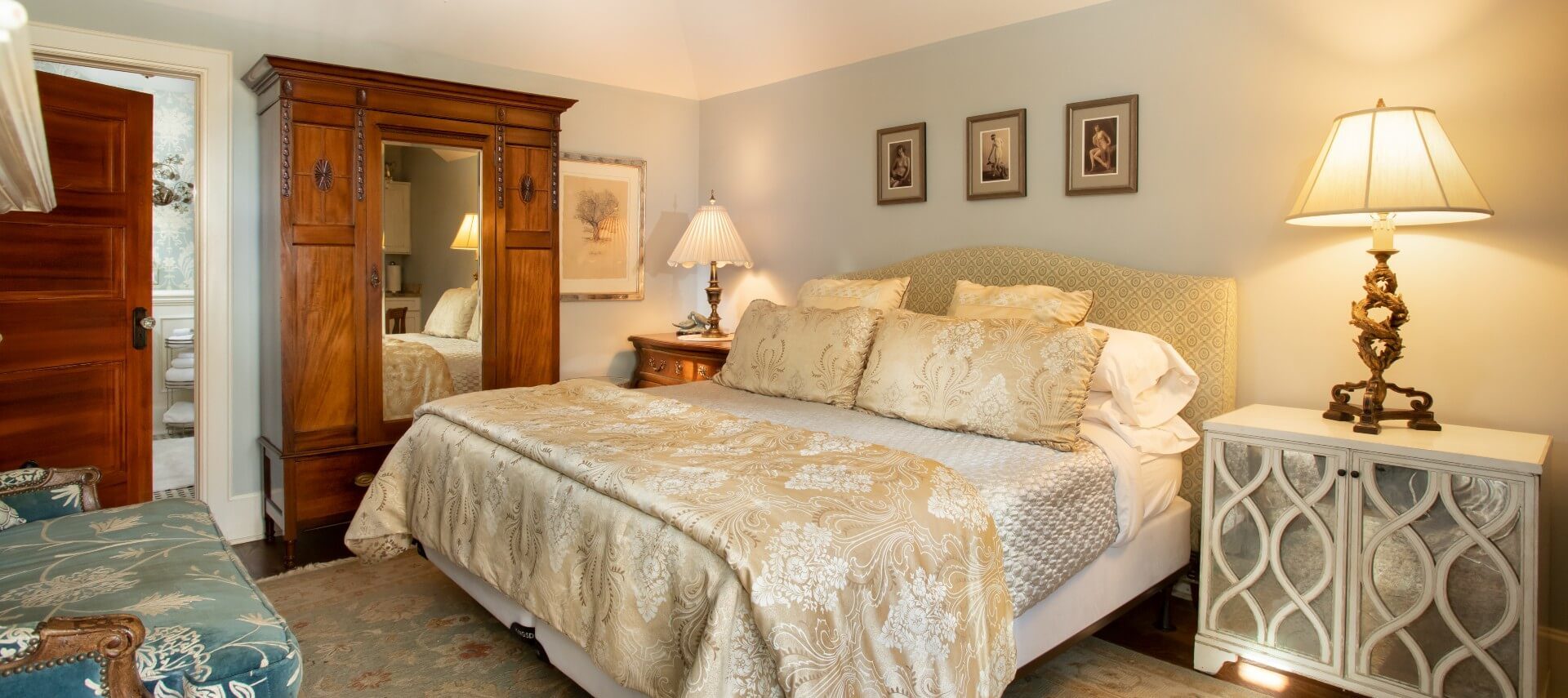 Bedroom with king size bed, tall armoire with mirror, sitting chair and bedside tables with lamps