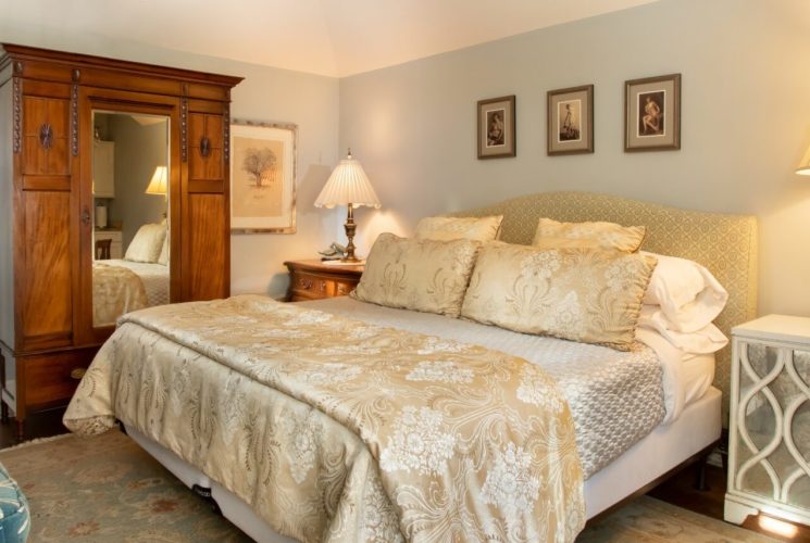 Bedroom with king size bed, tall armoire with mirror, sitting chair and bedside tables with lamps
